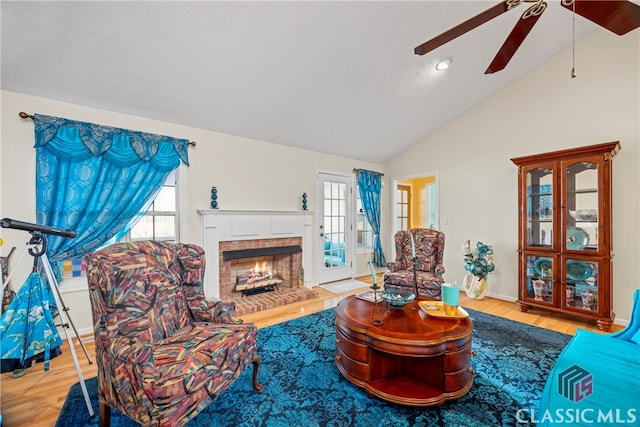 living room featuring french doors, lofted ceiling, a brick fireplace, light wood-type flooring, and ceiling fan