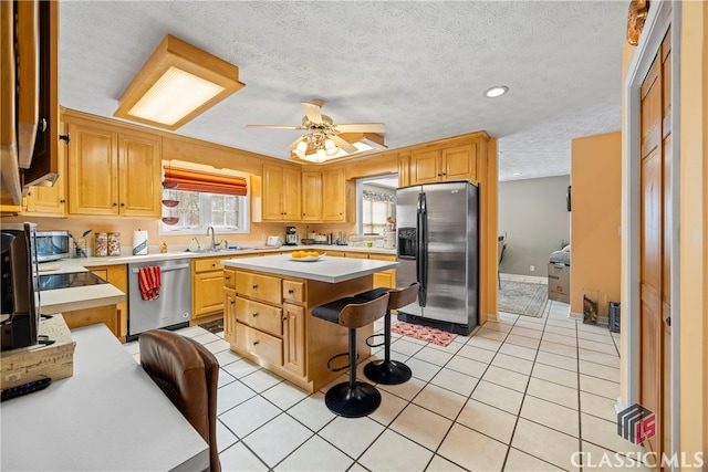 kitchen with appliances with stainless steel finishes, light tile patterned floors, a breakfast bar, a kitchen island, and sink