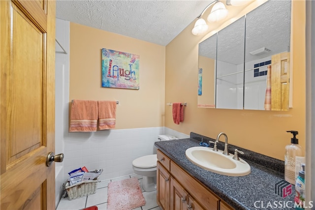 bathroom with a textured ceiling, tile patterned flooring, tile walls, toilet, and vanity