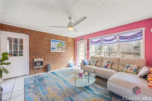 tiled living room featuring ceiling fan, a wood stove, heating unit, and brick wall