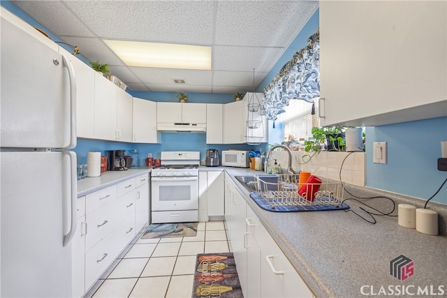 kitchen with white appliances, light tile patterned floors, a drop ceiling, white cabinets, and sink