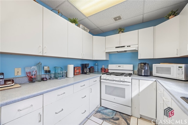 kitchen with white appliances, white cabinetry, light tile patterned flooring, and a drop ceiling