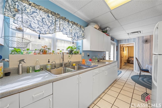 kitchen featuring light tile patterned floors, white refrigerator, a drop ceiling, white cabinets, and sink