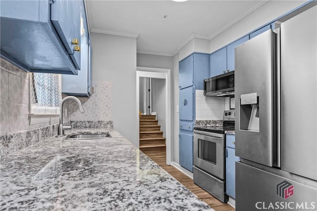 kitchen with appliances with stainless steel finishes, blue cabinetry, ornamental molding, sink, and backsplash