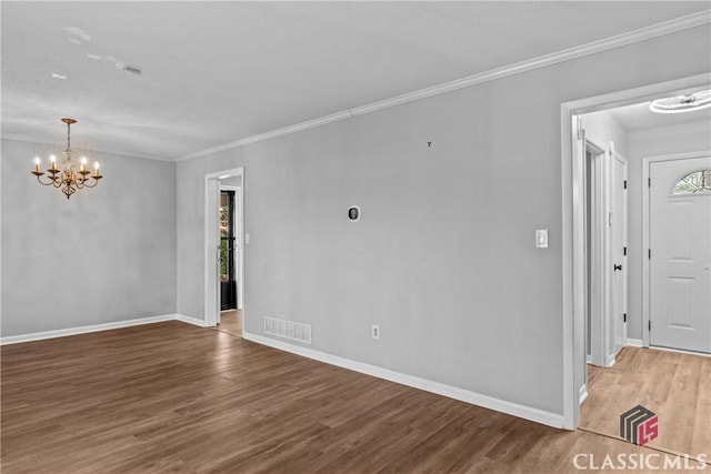 spare room featuring ornamental molding, hardwood / wood-style floors, and a notable chandelier