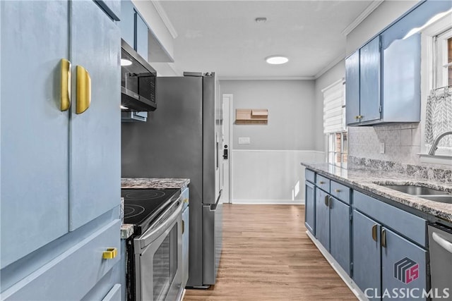 kitchen featuring appliances with stainless steel finishes, light hardwood / wood-style floors, blue cabinetry, ornamental molding, and sink