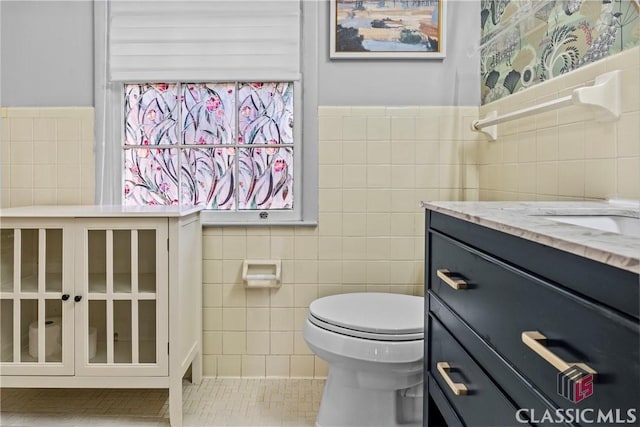 bathroom featuring toilet, tile patterned floors, vanity, and tile walls