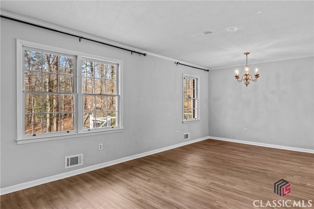 empty room featuring ornamental molding, a textured ceiling, hardwood / wood-style floors, and a notable chandelier