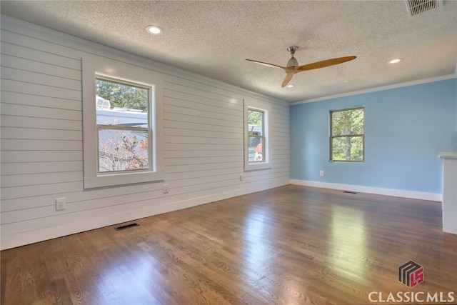 spare room featuring a textured ceiling, dark hardwood / wood-style flooring, wooden walls, and crown molding