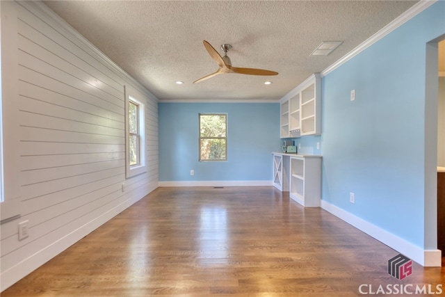 unfurnished living room with wooden walls, a textured ceiling, ceiling fan, ornamental molding, and hardwood / wood-style flooring