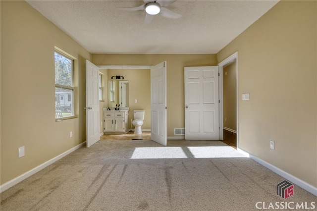 unfurnished bedroom featuring connected bathroom, a textured ceiling, ceiling fan, and light colored carpet