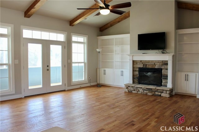 unfurnished living room featuring a stone fireplace, ceiling fan, french doors, beam ceiling, and light hardwood / wood-style flooring