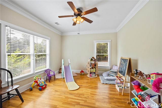 rec room with ceiling fan, a wealth of natural light, hardwood / wood-style flooring, and ornamental molding