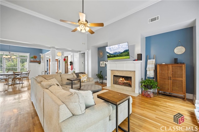 living room with ceiling fan with notable chandelier, hardwood / wood-style floors, ornamental molding, and a fireplace