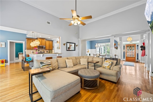 living room with light wood-type flooring, ornamental molding, and ceiling fan with notable chandelier