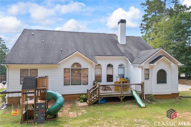 back of property with a lawn, a wooden deck, and a playground