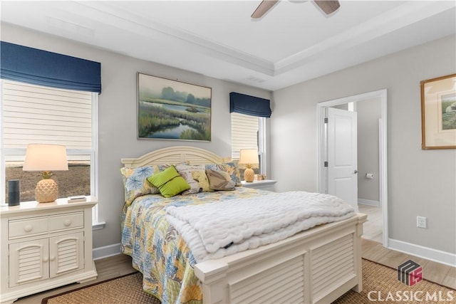 bedroom featuring ceiling fan, wood-type flooring, and a tray ceiling