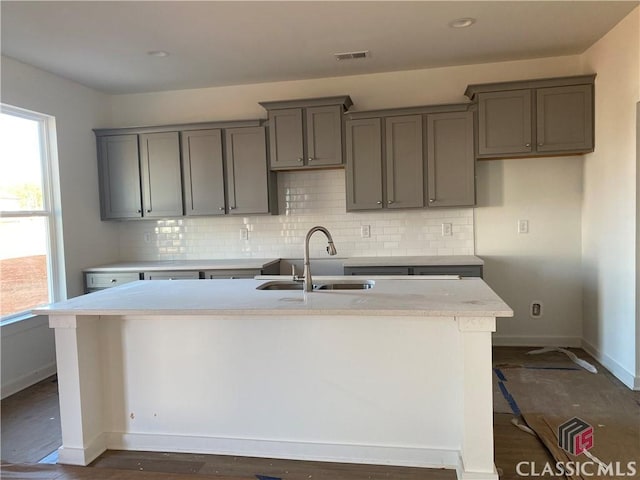 kitchen featuring gray cabinetry, decorative backsplash, sink, a kitchen breakfast bar, and a center island with sink