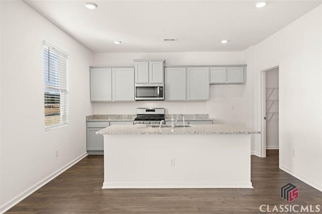 kitchen featuring sink, a kitchen island with sink, gray cabinetry, stainless steel appliances, and light stone counters