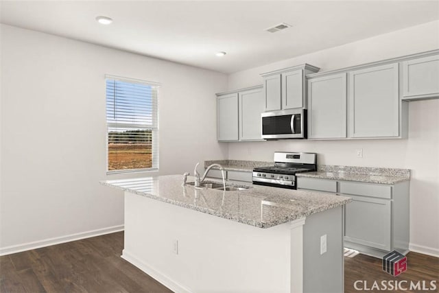 kitchen featuring a center island with sink, appliances with stainless steel finishes, gray cabinetry, light stone countertops, and sink