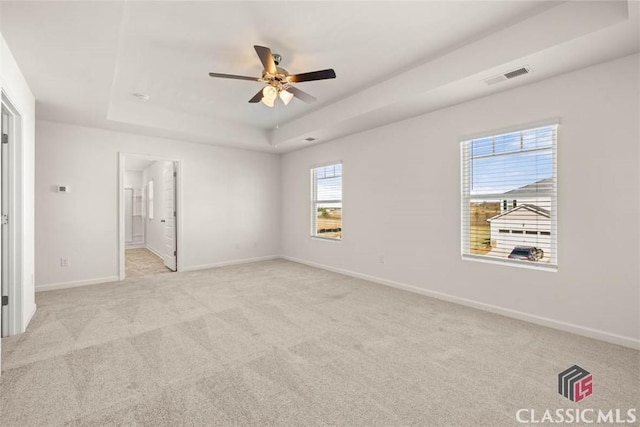 unfurnished bedroom featuring ceiling fan, light colored carpet, a tray ceiling, and ensuite bath