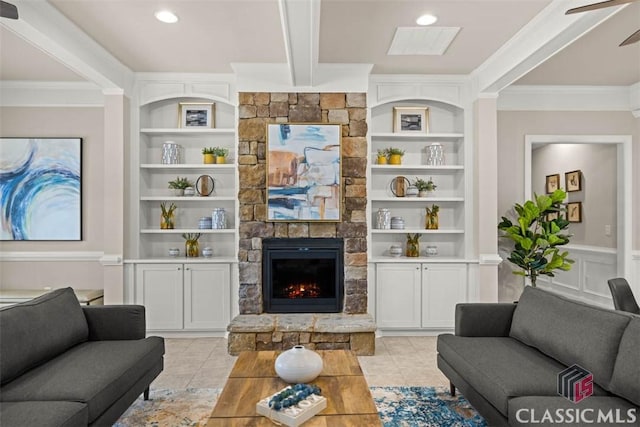 tiled living room with ceiling fan, built in shelves, a stone fireplace, and ornamental molding