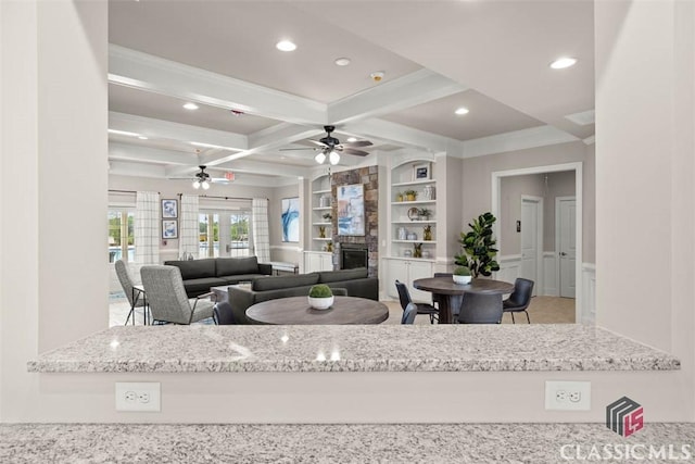 living room featuring coffered ceiling, ceiling fan, a fireplace, built in features, and beamed ceiling