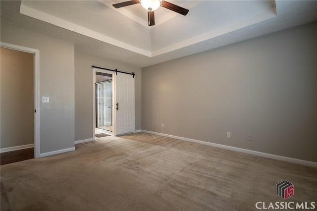 empty room featuring a raised ceiling, a barn door, ceiling fan, and light colored carpet