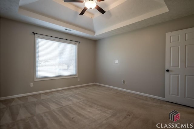 spare room featuring ceiling fan, light colored carpet, and a tray ceiling