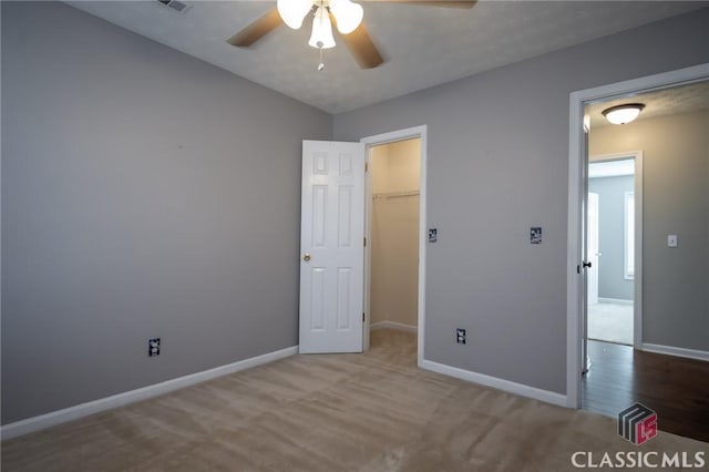 unfurnished bedroom featuring ceiling fan, a walk in closet, a closet, and light colored carpet