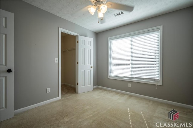 unfurnished bedroom featuring a spacious closet, a textured ceiling, a closet, ceiling fan, and light colored carpet