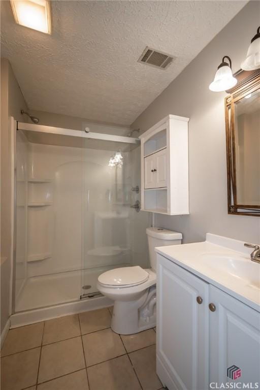 bathroom featuring toilet, vanity, tile patterned flooring, a textured ceiling, and a shower with door