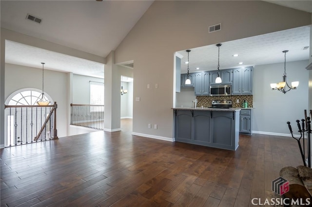 kitchen featuring tasteful backsplash, an inviting chandelier, hanging light fixtures, dark wood-type flooring, and stainless steel appliances