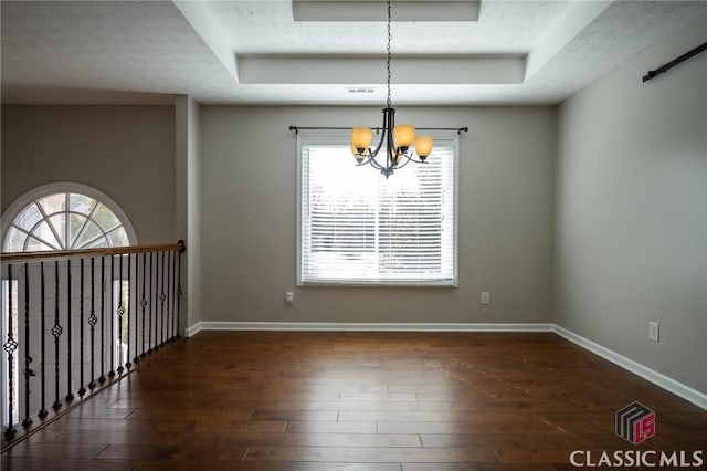 empty room featuring a textured ceiling, dark wood-type flooring, a tray ceiling, and a notable chandelier