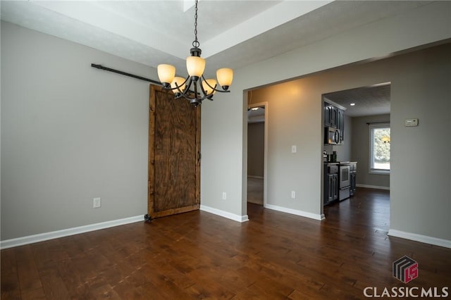 empty room with a barn door, dark hardwood / wood-style floors, and a chandelier