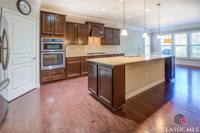 kitchen with an island with sink, sink, hanging light fixtures, light stone counters, and custom range hood