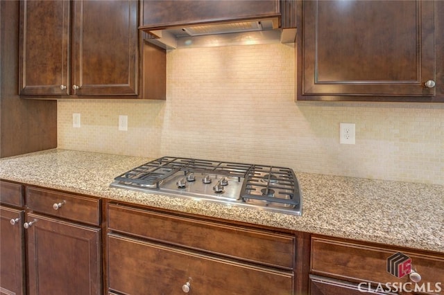 kitchen with dark brown cabinetry, tasteful backsplash, premium range hood, light stone counters, and stainless steel gas stovetop