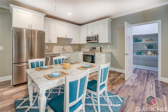 kitchen featuring stainless steel appliances, backsplash, white cabinets, light hardwood / wood-style flooring, and sink