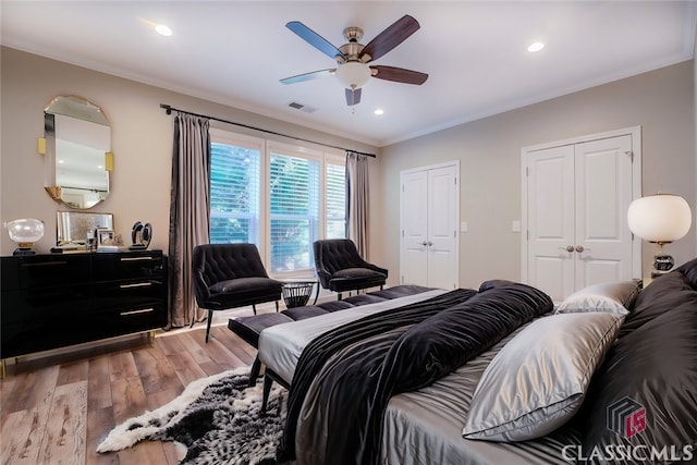 bedroom featuring ceiling fan, crown molding, light hardwood / wood-style flooring, and multiple closets