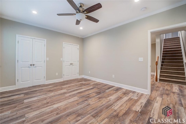 unfurnished bedroom featuring ceiling fan, wood-type flooring, ornamental molding, and two closets