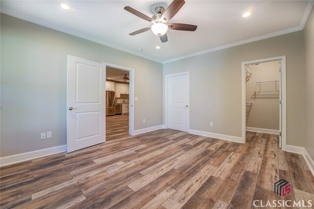 unfurnished bedroom featuring ceiling fan, stainless steel refrigerator, a spacious closet, ornamental molding, and a closet