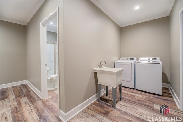 laundry area with light hardwood / wood-style floors, ornamental molding, and washing machine and dryer