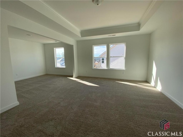 empty room featuring ornamental molding, dark carpet, and a tray ceiling