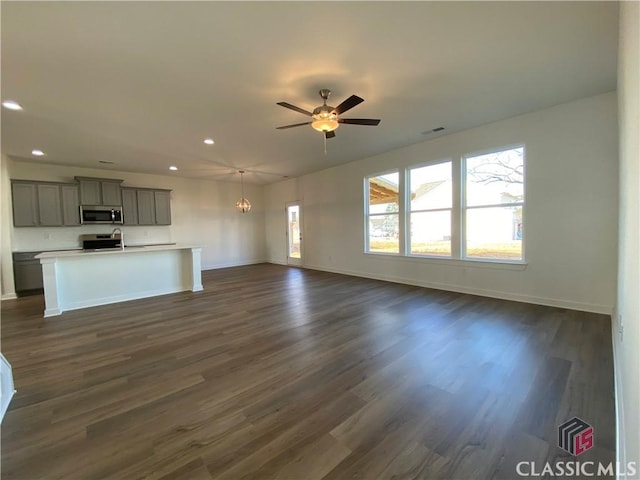 unfurnished living room with dark wood-type flooring, a wealth of natural light, and ceiling fan with notable chandelier