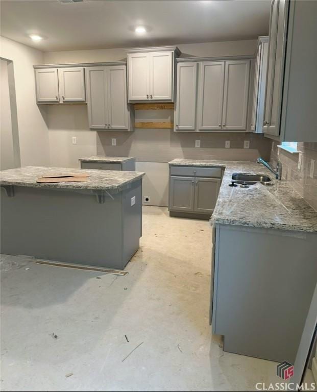 kitchen with sink, light stone counters, and gray cabinets