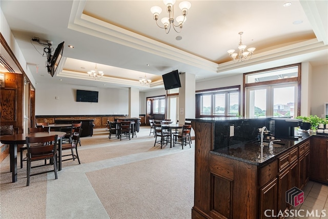 kitchen featuring a tray ceiling, light colored carpet, hanging light fixtures, dark stone counters, and a chandelier