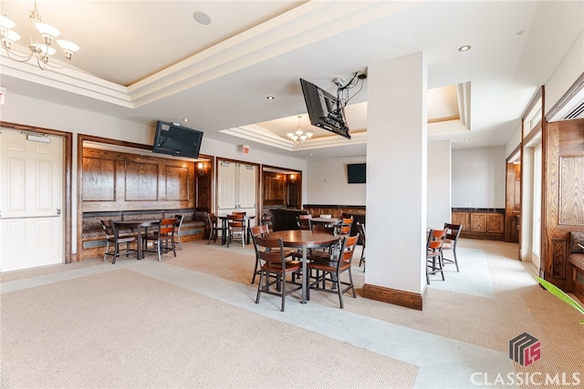 dining area with a tray ceiling, light carpet, and an inviting chandelier