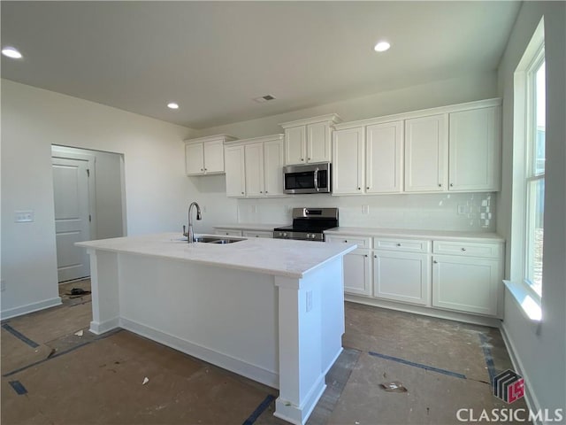 kitchen with a wealth of natural light, appliances with stainless steel finishes, white cabinetry, and a kitchen island with sink