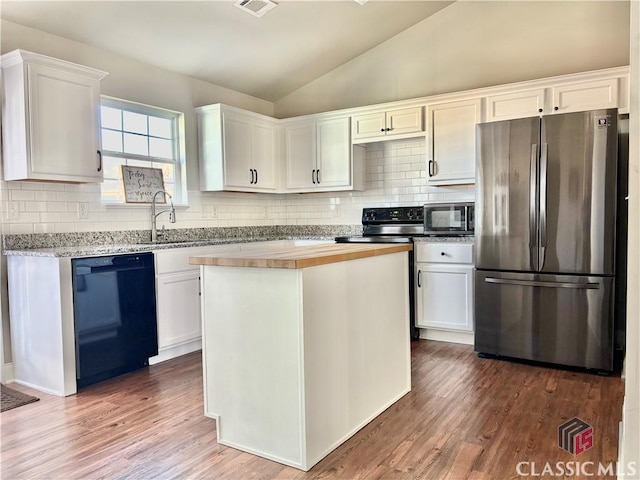 kitchen featuring vaulted ceiling, black dishwasher, white cabinets, and stainless steel refrigerator