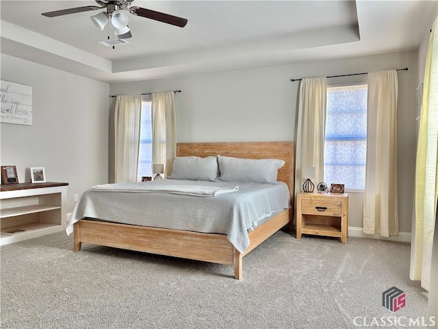 carpeted bedroom with a raised ceiling and ceiling fan